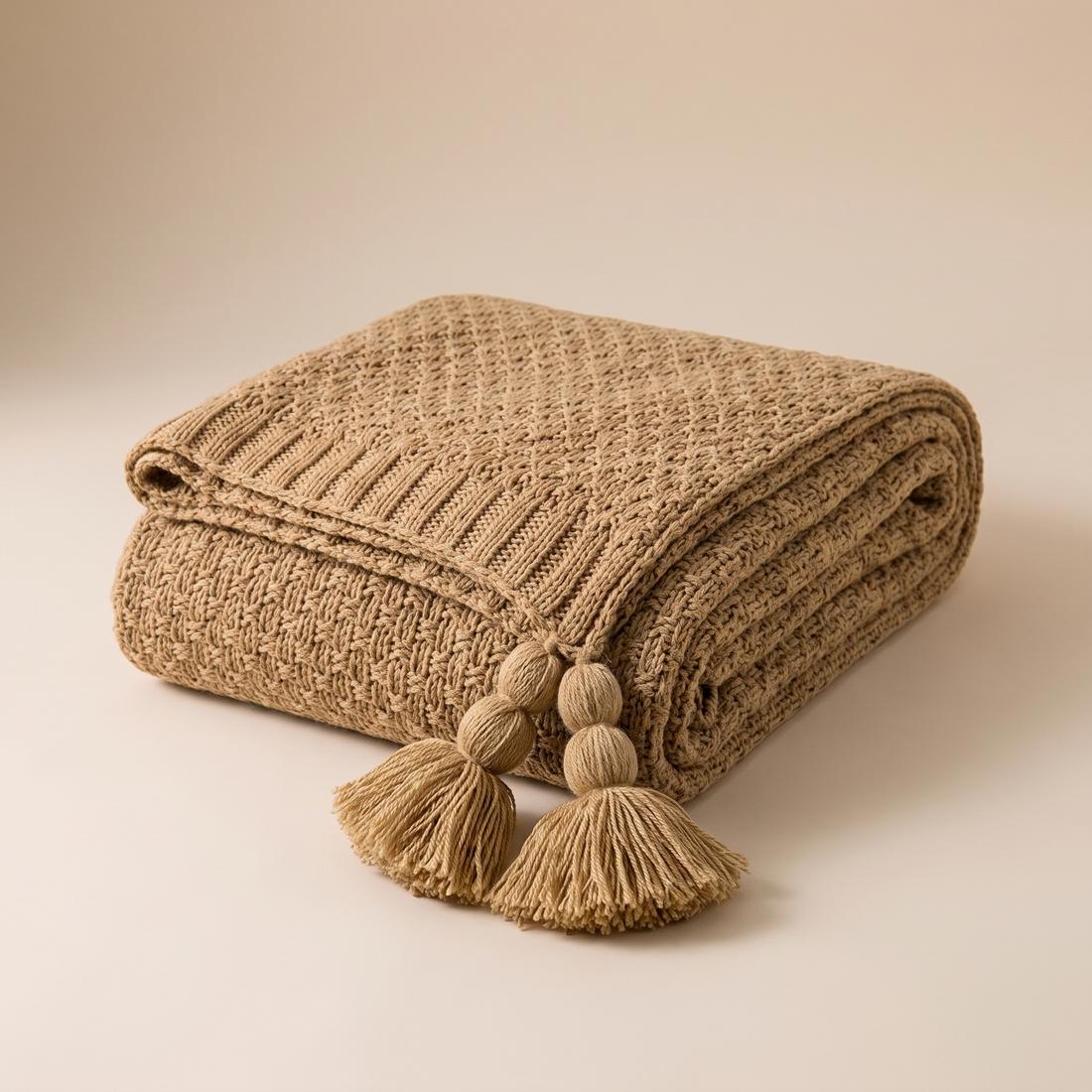 A soft neutral chunky knit throw folded over an armchair in a warm, low-lit living room, the picture of a cozy space