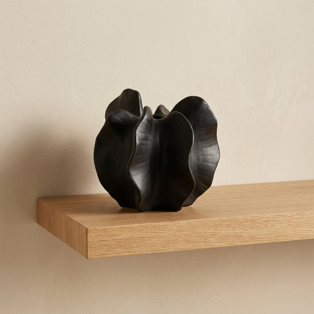 Matte black ceramic sculptural bloom-form vase styled on a floating oak shelf