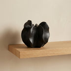 Matte black ceramic sculptural bloom-form vase styled on a floating oak shelf