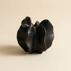 Matte black speckled ceramic wabi-sabi bloom vase with ruffled petal lobes and central cleft, on a warm-white studio backdrop