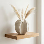 Cream ceramic bloom vase holding dried pampas stems on a floating oak shelf