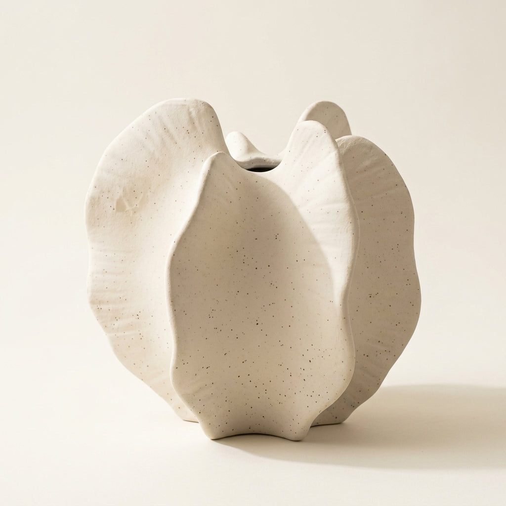 Cream speckled matte ceramic wabi-sabi bloom vase with ruffled petal lobes and central cleft, on a warm-white studio backdrop
