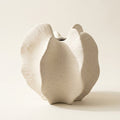 Cream speckled matte ceramic wabi-sabi bloom vase with ruffled petal lobes and central cleft, on a warm-white studio backdrop