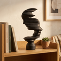 Black abstract mask-profile resin sculpture on a study bookcase shelf