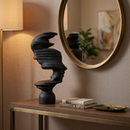 Black abstract mask-profile resin sculpture on an entryway console below a mirror