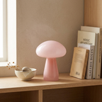 Pink glass mushroom atmosphere table lamp on a wooden shelf beside books and a ceramic bowl