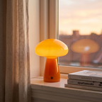 Orange glass mushroom table lamp glowing on a windowsill beside a linen curtain at sunset