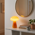 Orange glass mushroom atmosphere table lamp glowing softly on a marble console table beneath a round mirror