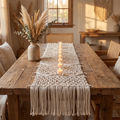 Cream bohemian macramé table runner with a row of tea-lights and pampas on a reclaimed-wood table