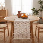 Cream bohemian macramé runner on a round rattan table with a terracotta jug and oranges