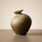 Sandstone stoneware bottle vase, low three-quarter hero angle on a warm-taupe surface
