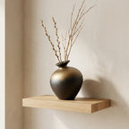 Bronze-gold gradient stoneware bottle vase with tall dried branches on a floating oak shelf
