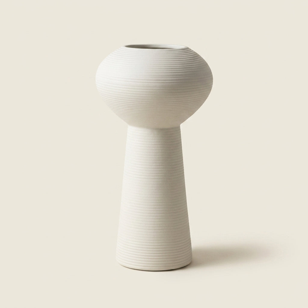 Matte white fine-ribbed ceramic Nordic vase, footed pedestal hourglass shape, on a warm-white studio background