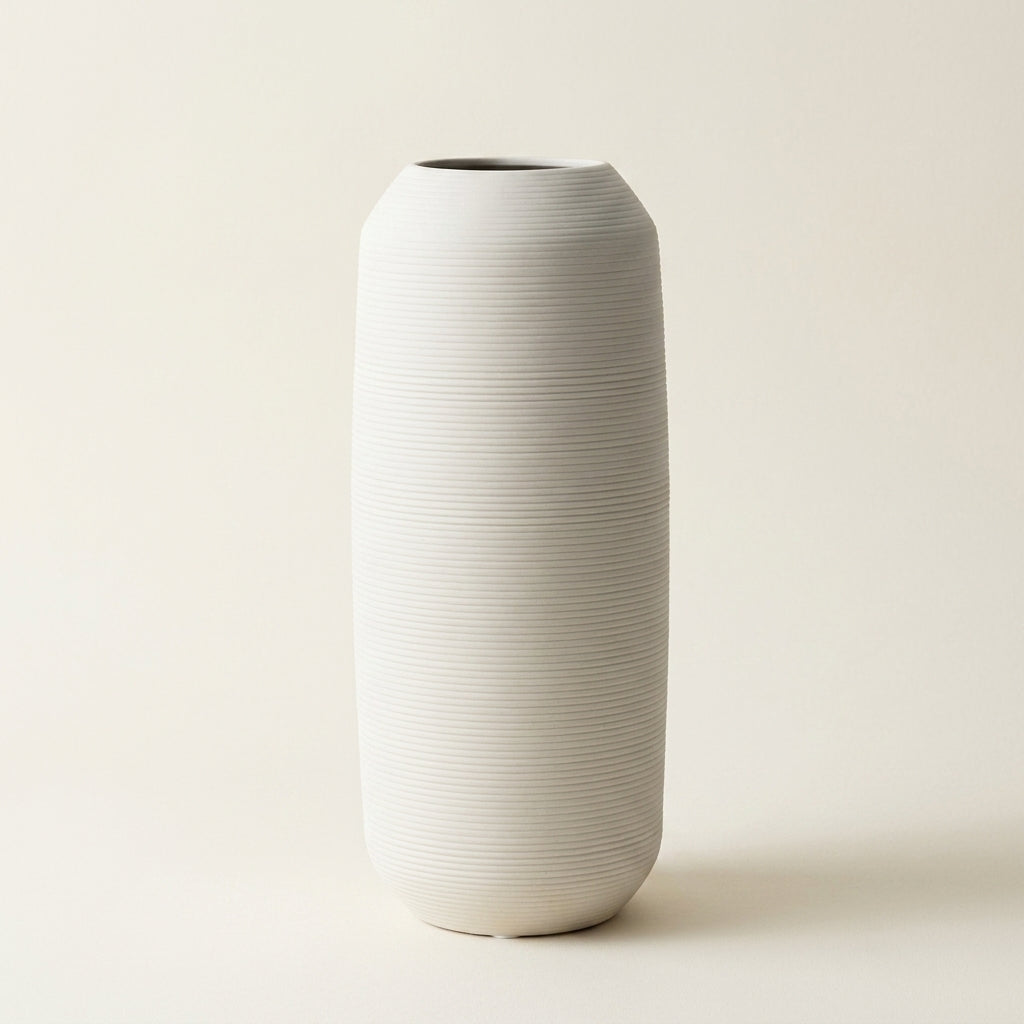 Matte white fine-ribbed ceramic Nordic vase, tall tapered shape, on a warm-white studio background