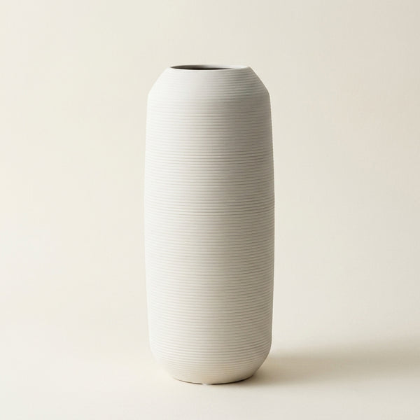 Matte white fine-ribbed ceramic Nordic vase, tall tapered shape, on a warm-white studio background