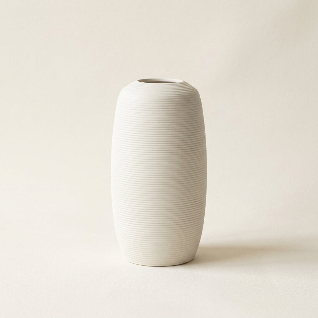 Matte white fine-ribbed ceramic Nordic vase, rounded barrel shape, on a warm-white studio background