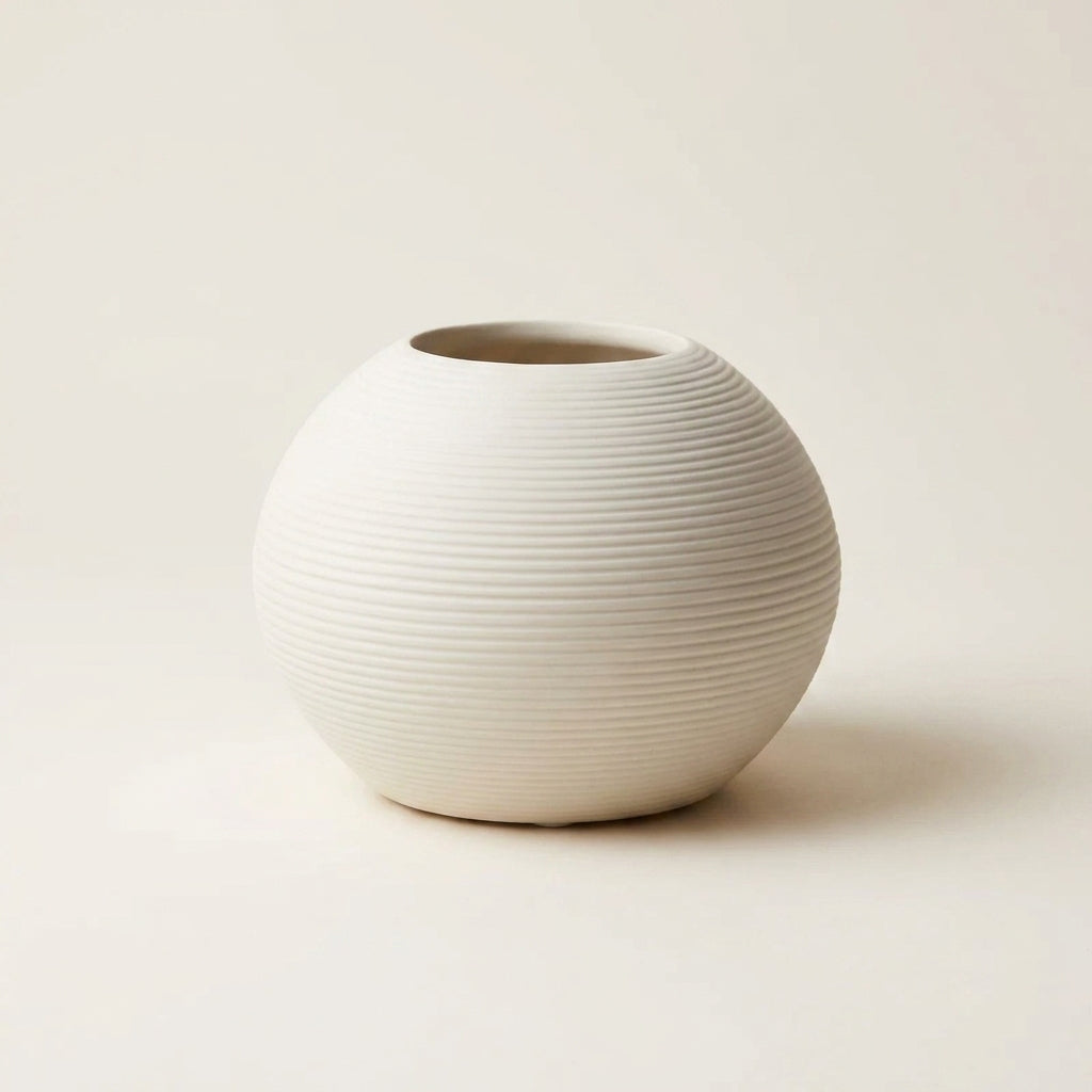 Matte white fine-ribbed ceramic Nordic vase, round squat orb shape, on a warm-white studio background