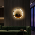 Black ring wall lamp with wooden shelf glowing warm on a dark accent wall