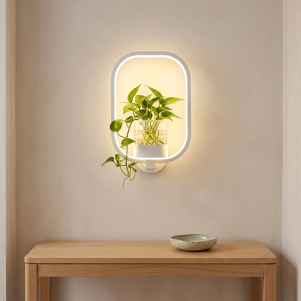 White oblong-frame wall lamp with a glass plant vase above an entryway console