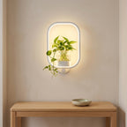 White oblong-frame wall lamp with a glass plant vase above an entryway console