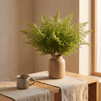 Minimalist tabletop with a single faux fern bunch and stoneware mug