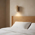 Wabi-Sabi travertine wall lamp — above oak headboard with linen bedding