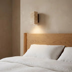 Wabi-Sabi travertine wall lamp — above oak headboard with linen bedding