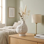 White ceramic face vase with dried stems on a bedroom dresser