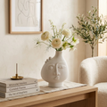 White ceramic face vase holding white ranunculus on a console table