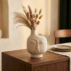 White ceramic face vase holding dried pampas on a wooden dining sideboard