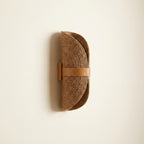 Curled half-moon woven rattan-look fiber wall sconce in warm tan with a leather-look strap mount.