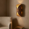 Curled woven sconce in a styled interior, beside a bed or reading chair, warm ambient light.