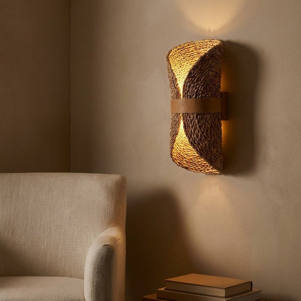 Curled woven sconce in a styled interior, beside a bed or reading chair, warm ambient light.