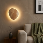 Oval wood pebble wall light with warm halo on a living room accent wall