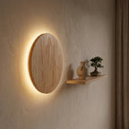 Round natural wood disc wall light mounted cleanly on an accent wall with a floating shelf and warm backlit halo