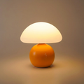 Mushroom table lamp with a warm cream shade and glossy orange base, glowing warmly on a clean background
