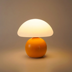 Mushroom table lamp with a warm cream shade and glossy orange base, glowing warmly on a clean background