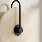 Close-up of the alabaster-look glowing disc and dark center hub of the wall sconce