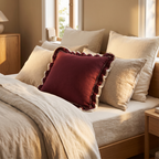 Wine red woven cushion cover with frill edge on a bed