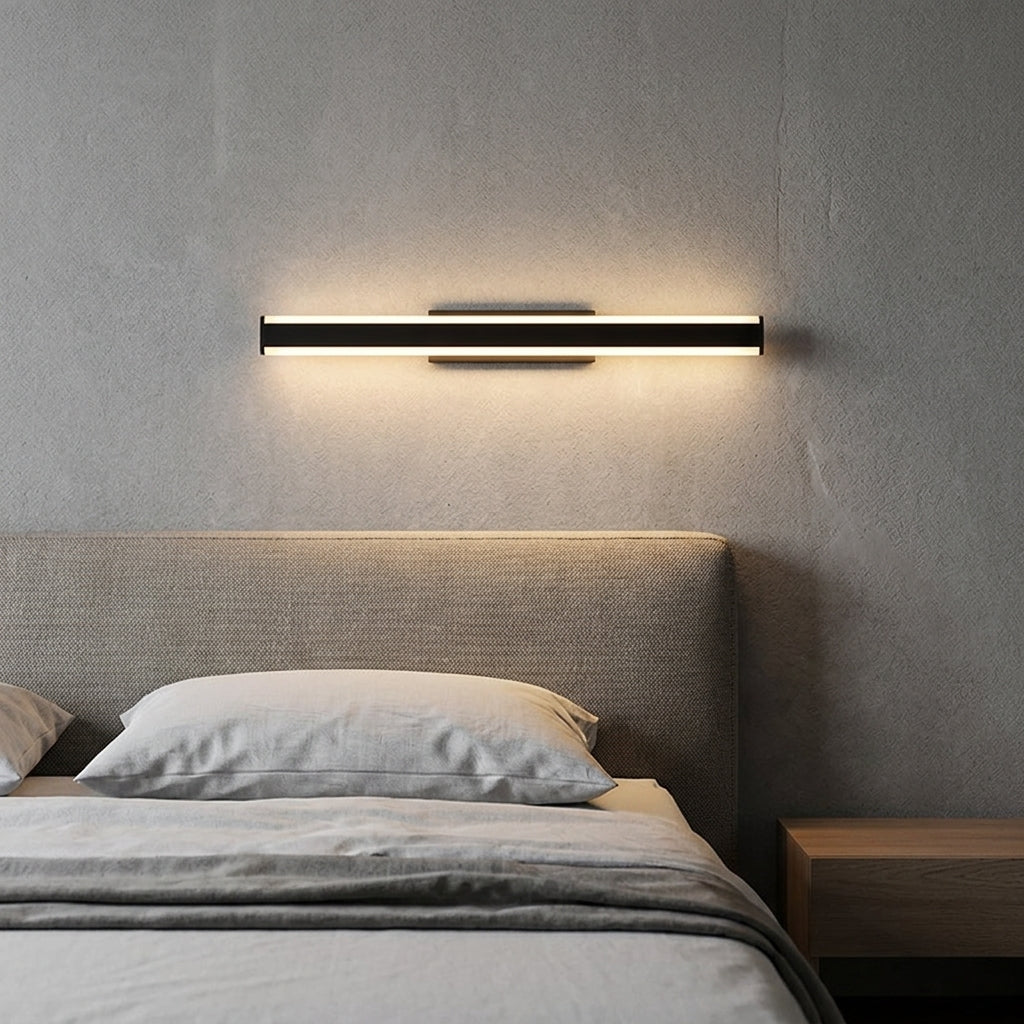 Short black linear LED bar mounted horizontally above a bed headboard, warm glow