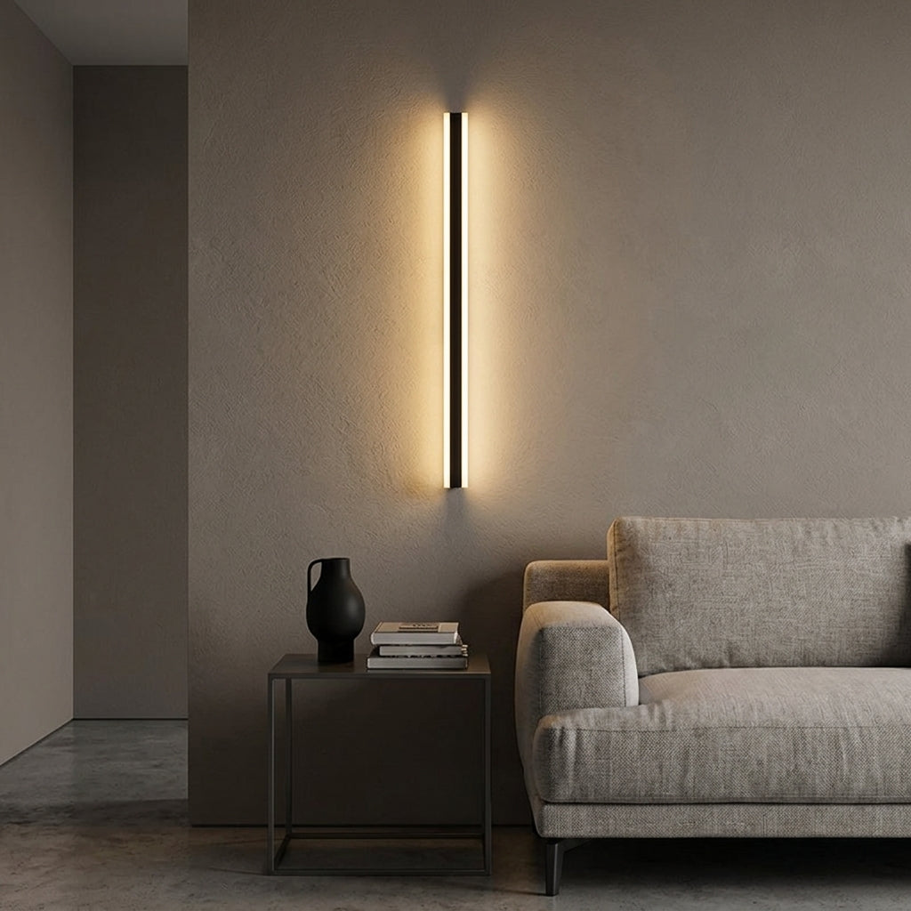 Short black linear LED bar wall light beside a sofa in a living room, warm evening glow
