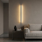 Short black linear LED bar wall light beside a sofa in a living room, warm evening glow