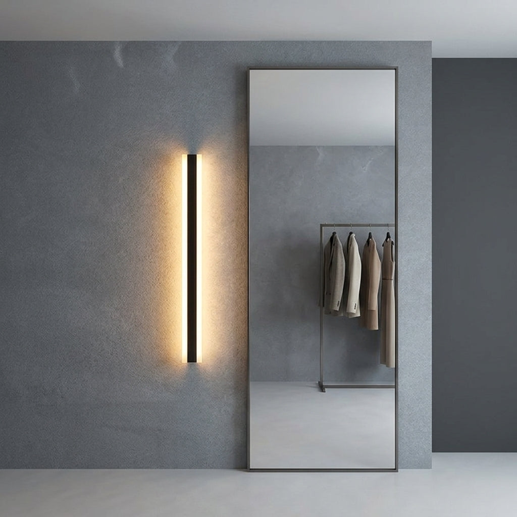 Short black linear LED bar wall light beside a full-length mirror in a dressing area, warm glow