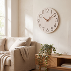 Light whitewashed wood minimalist wall clock with cut-out numerals and branch hands in a living room