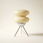 Cream glass macaron table lamp styled with books and decor as a sculptural accent piece.
