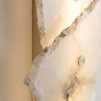 Stacked stone-look wall sconce mounted beside a mirror with a soft ambient glow.