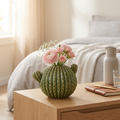 Green cactus-shaped ceramic vase holding pink ranunculus on a bedroom nightstand