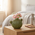 Green cactus-shaped ceramic vase holding pink ranunculus on a bedroom nightstand