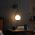 Black teardrop wall sconce with frosted glass globe glowing warm above a nightstand