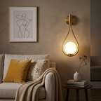 Gold teardrop globe wall sconce on a living room accent wall beside a sofa